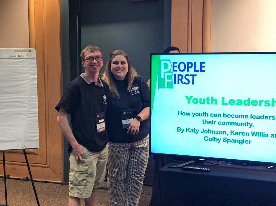 People stand next to TV with People First presentation